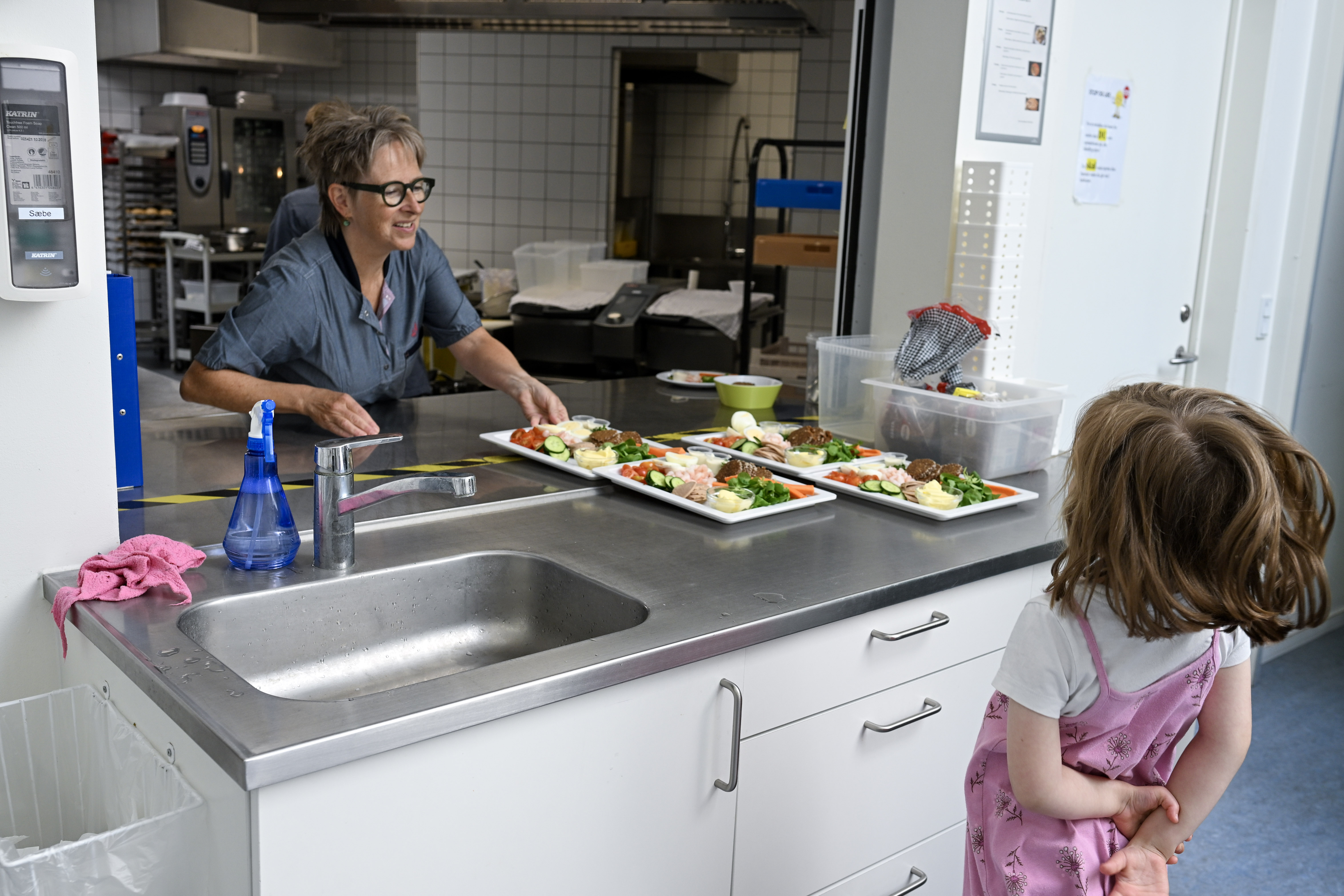 Voksen stiller mad frem på bord, mens et barn kigger på