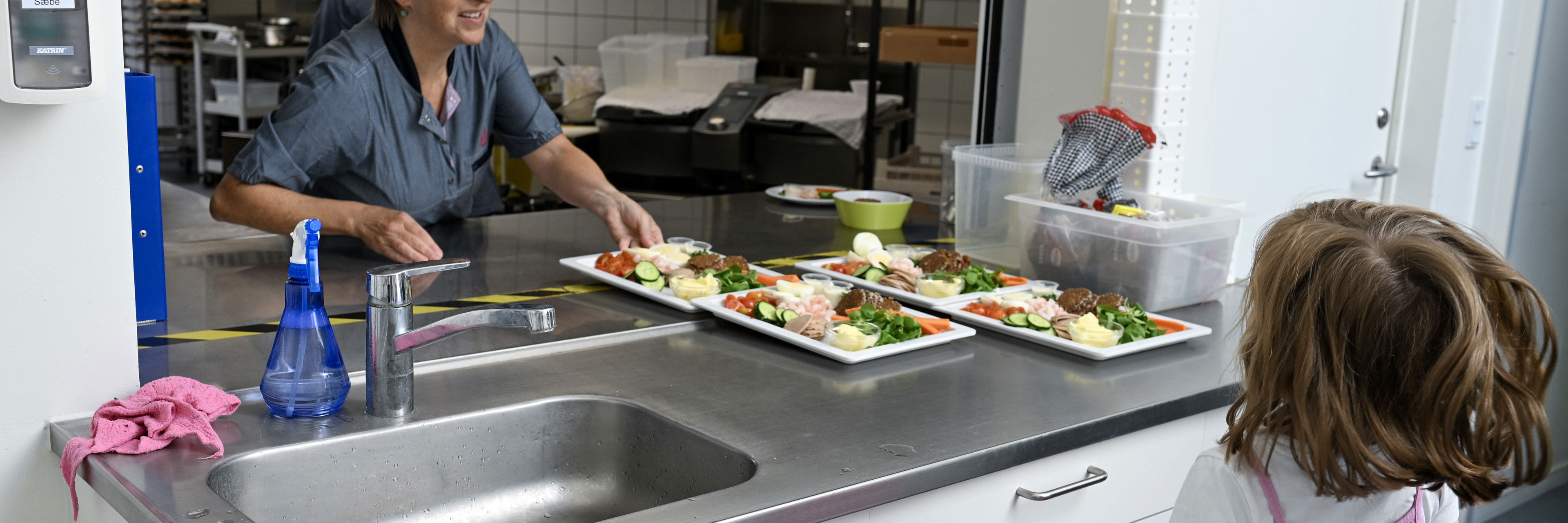 Voksen stiller mad frem på bord, mens et barn kigger på