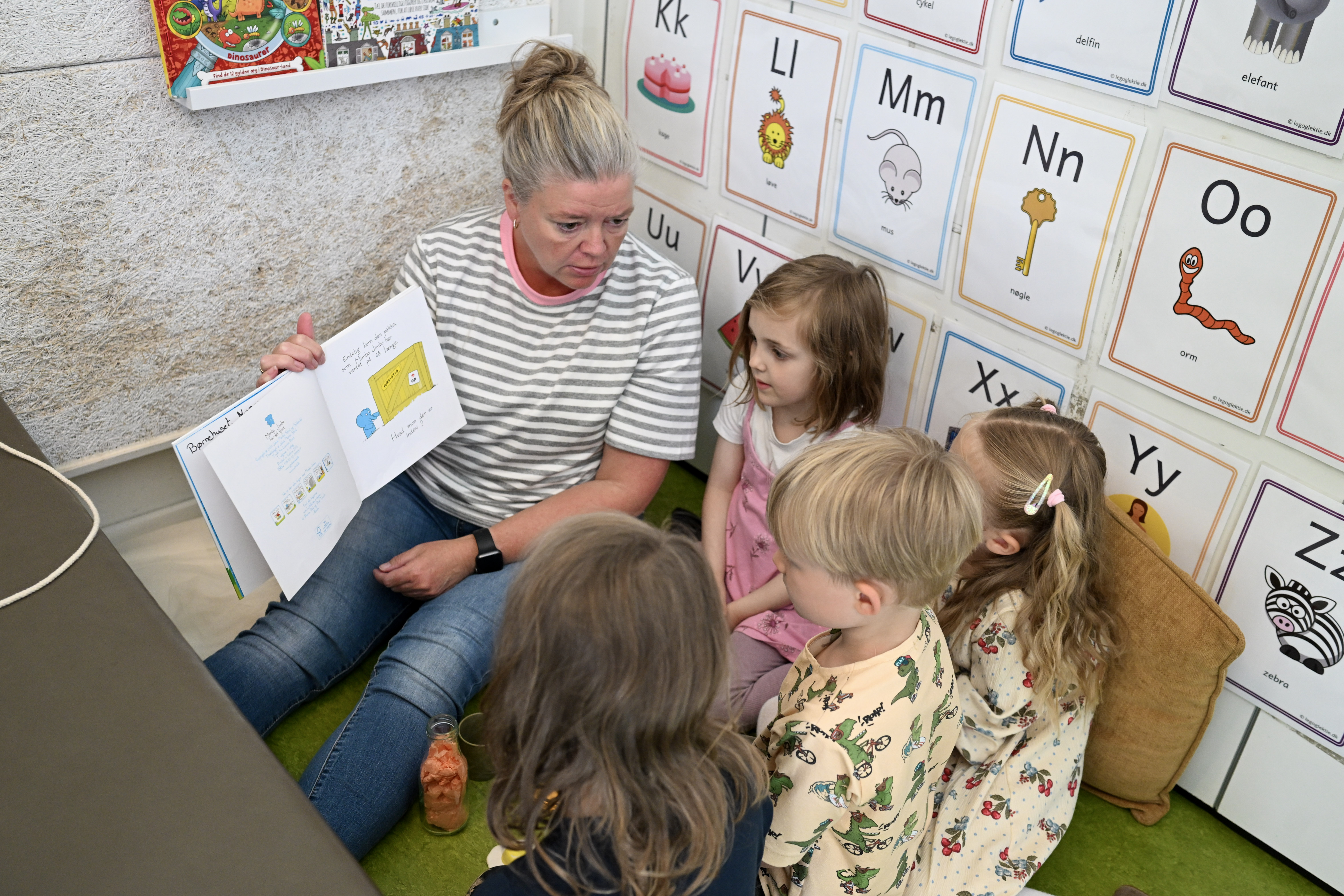 Voksen læser bog for børn og viser dem billeder deri